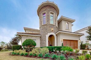 Una casa de dos pisos con una torre de piedra, un garaje y un jardín bien cuidado.