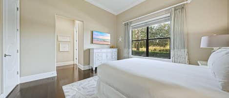 A bedroom with a large bed, a dresser, a television, and a window with curtains.