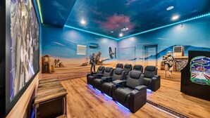 Ein Heimkino mit einem Wüsten-Wandbild, verschiedenen Sitzgelegenheiten und einem Projektor.