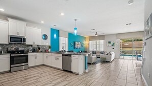 A modern kitchen with white cabinets, a central island, stainless steel appliances, and a blue accent wall. - Bright Villa with Theater in Champions Gate (Davenport)