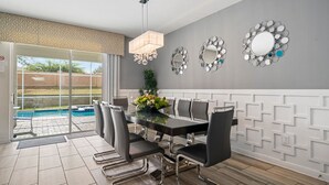 A dining area with a glass-top table, black chairs, and a decorative mirror on the wall. - Bright Villa with Theater in Champions Gate (Davenport)