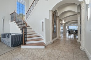 A spacious interior with a wooden staircase, a gray sofa, and a view through an arched doorway.