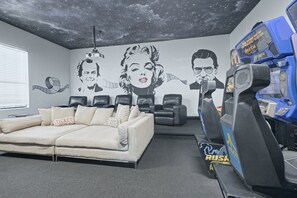 A room with a sofa, a wall mural, and a gaming machine.