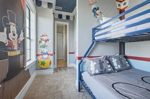 A child's bedroom with bunk beds, a wall mural, and a door leading to another room.