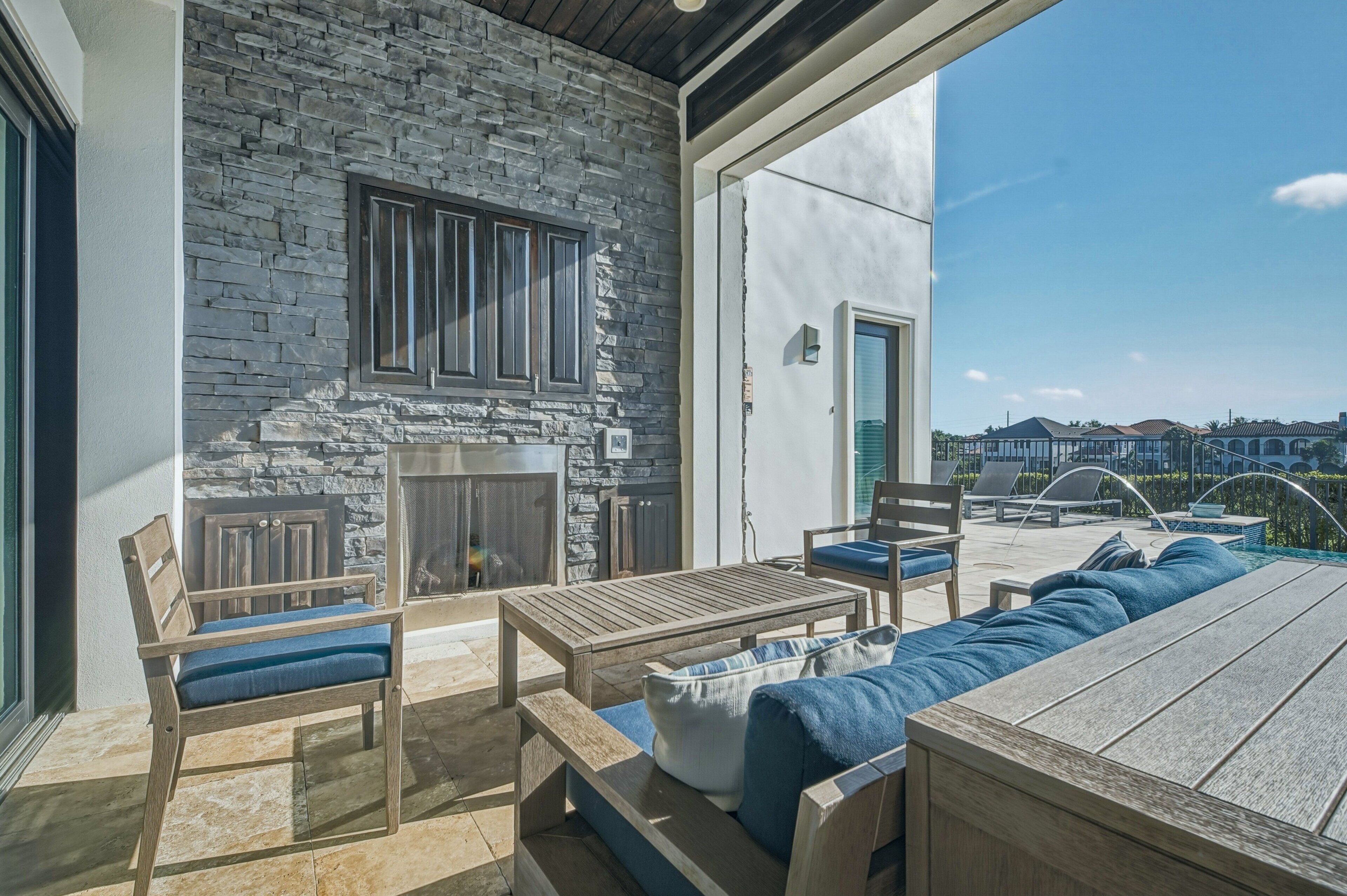 Eine Terrasse mit Steinmauern, Kamin, Sitzgelegenheiten und Blick auf benachbarte H äuser.