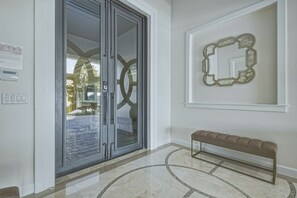 Un couloir avec un banc, une porte dotée d’un panneau en verre et un miroir fixé au mur.