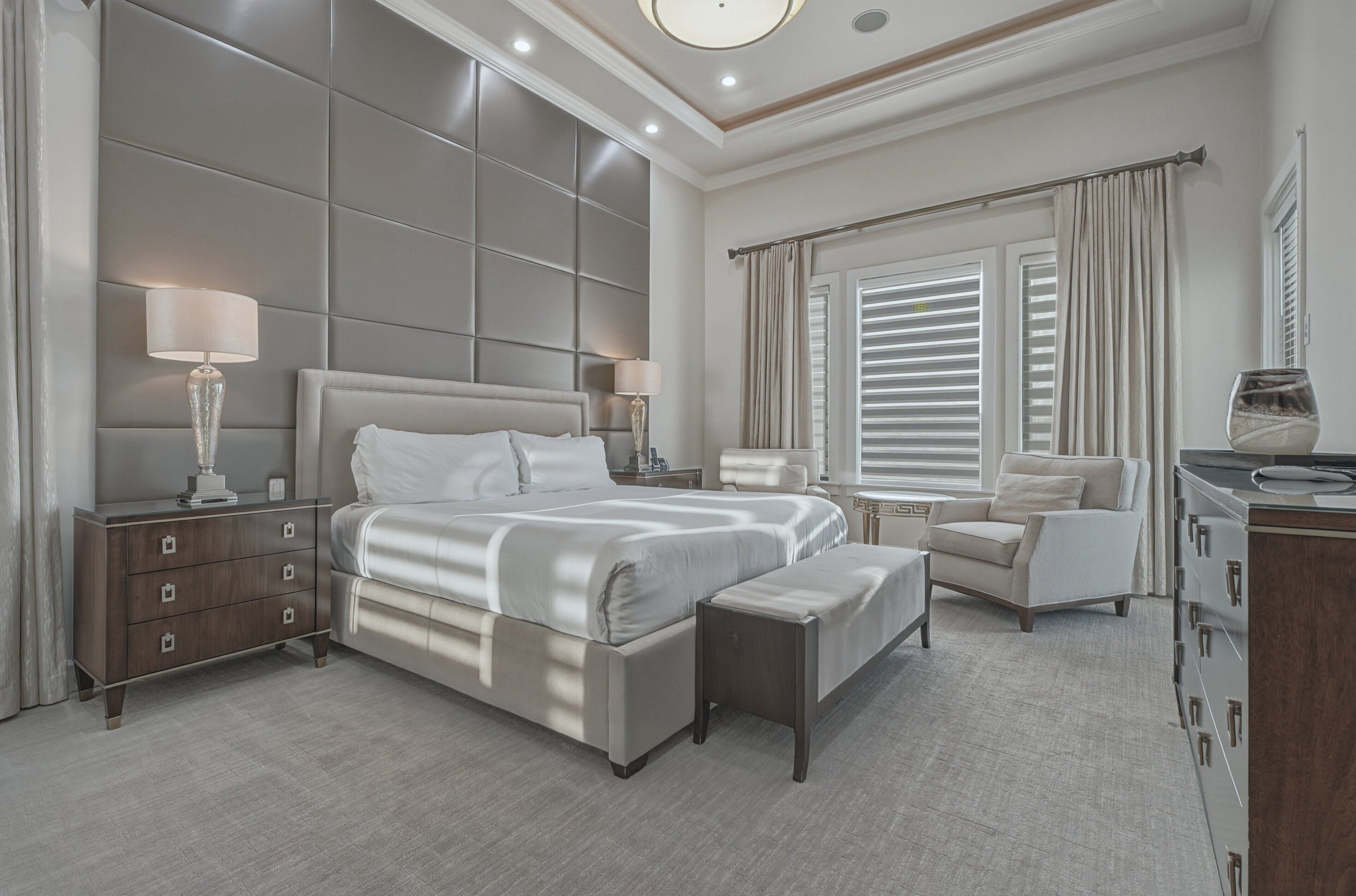 A modern bedroom with a large bed, bedside tables, a chair, and a dresser.