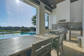 Eine moderne Außenküche mit Blick auf den Pool, einer Holzterrasse und einem Essbereich.