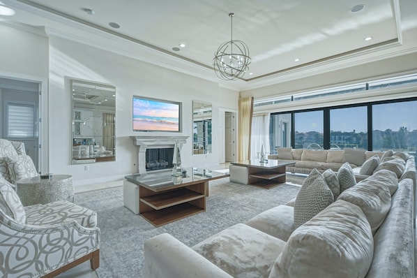 A spacious living room with a large sofa set, a fireplace, and a television mounted on the wall. - Sun-Filled Haven with Sports Themed Game Room at Reunion (Reunion)