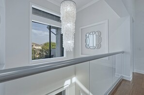 Un interior moderno con barandilla de vidrio, un candelabro y un elemento decorativo en la pared.