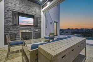An outdoor seating area with a stone wall, a fireplace, and a television screen. - Sun-Filled Haven with Sports Themed Game Room at Reunion (Reunion)