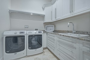 Un lavadero pequeño con dos lavadoras Maytag, un lavabo blanco y una encimera de granito.