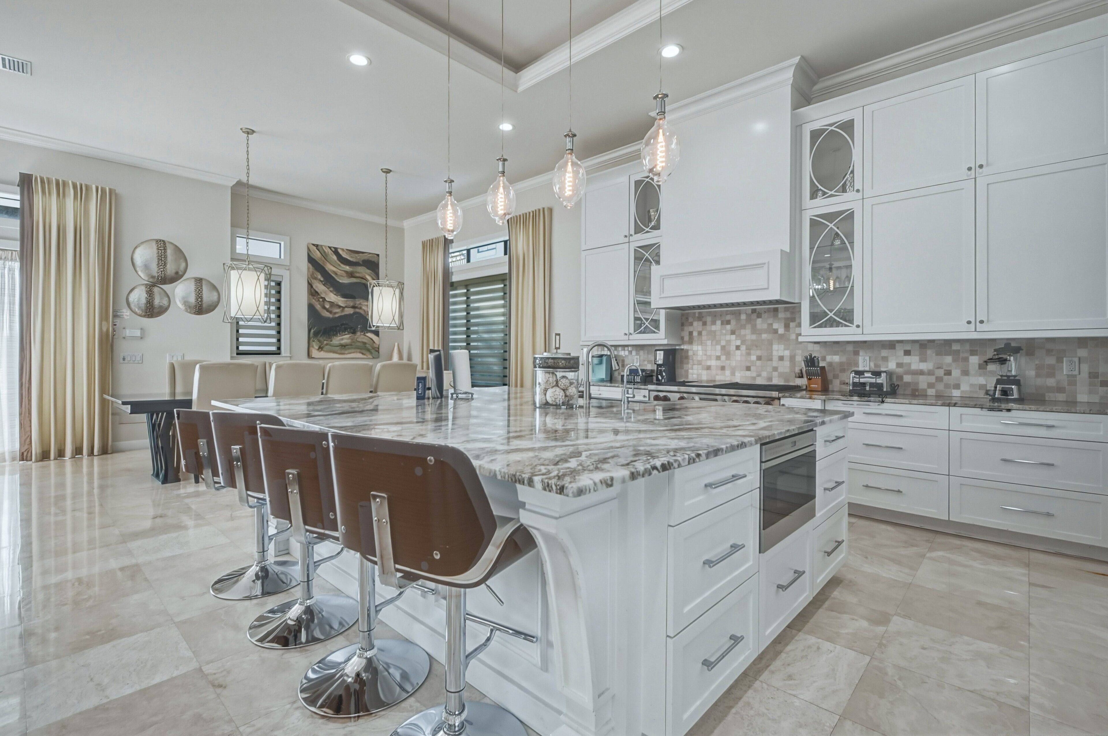 A modern kitchen with a marble island, bar stools, and pendant lighting.