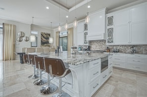 A modern kitchen with a marble island, bar stools, and pendant lighting. - Sun-Filled Haven with Sports Themed Game Room at Reunion (Reunion)