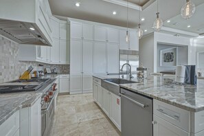 A modern kitchen with white cabinetry, a stainless steel range, and a marble countertop. - Sun-Filled Haven with Sports Themed Game Room at Reunion (Reunion)