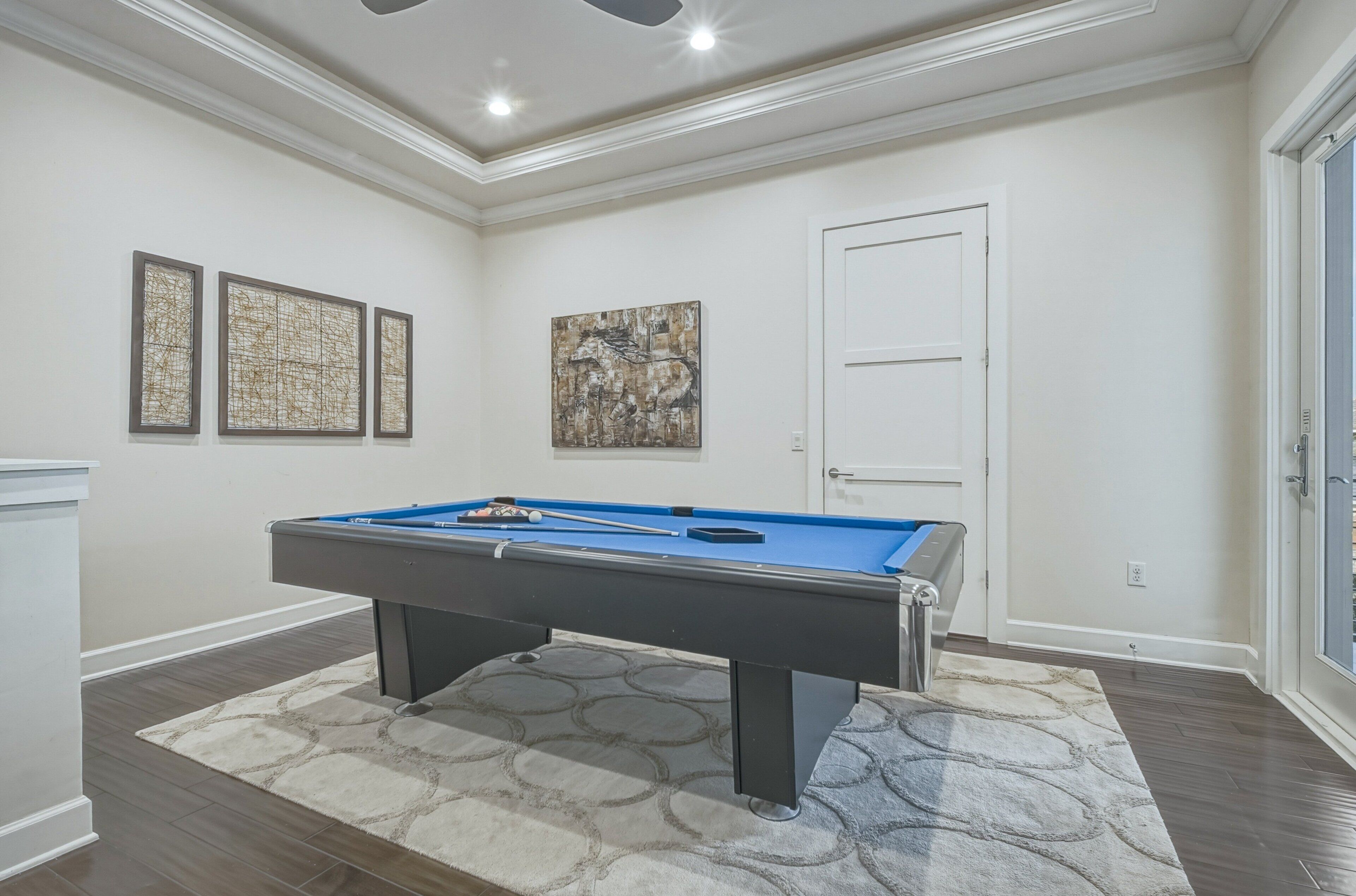 A pool table in a room with white walls, a door, and three framed artworks.