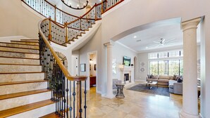 A spacious living area with a grand staircase, a fireplace, and a large window providing natural light. - Luxury Villa with Elegant Living Space at Reunion (Kissimmee)