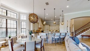 A spacious kitchen with a central island, large windows, and a staircase leading to another level. - Luxury Villa with Elegant Living Space at Reunion (Kissimmee)