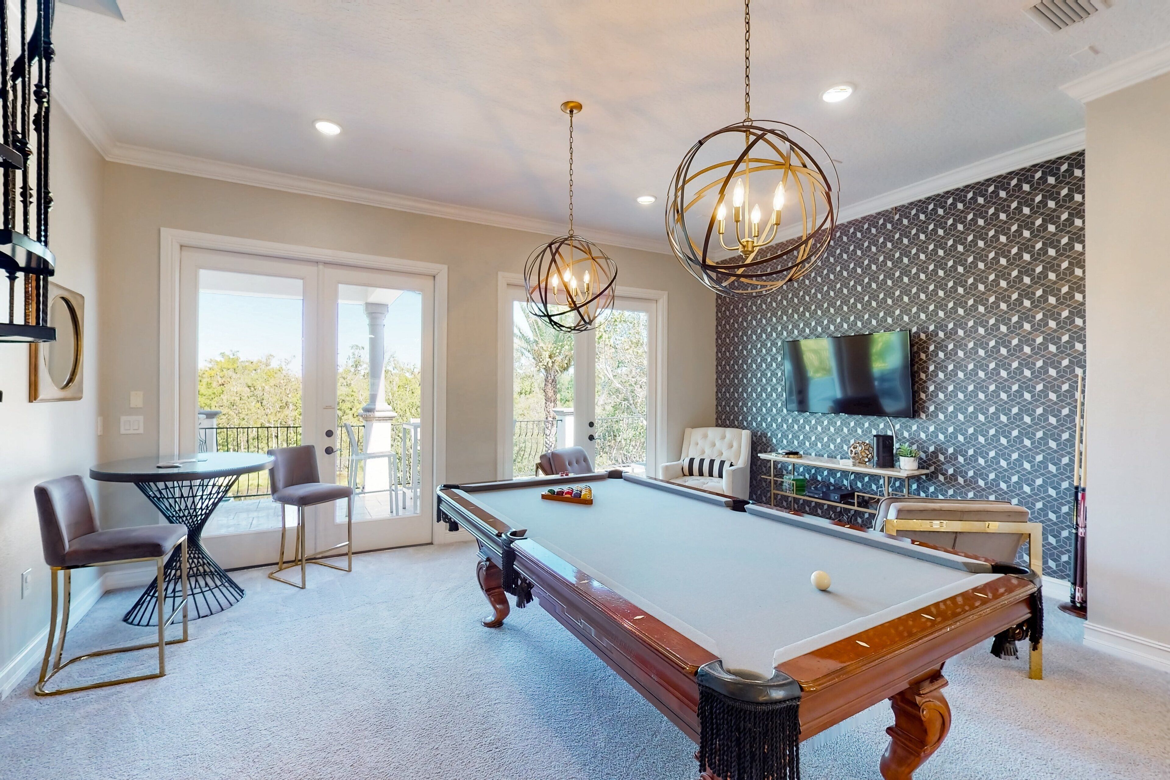 A pool table with chairs, a television, and a patterned wall.