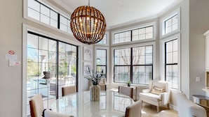 A spacious dining area with a glass table, white chairs, and a large window with multiple panes. - Luxury Villa with Elegant Living Space at Reunion (Kissimmee)