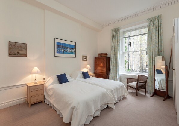 A bedroom with two beds, a wooden dresser, a chair, a window with curtains, and a mirror.