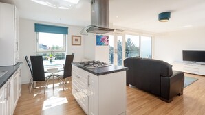 Et moderne køkken med en central ø, et spiseområde med stole, en sofa og et fjernsyn i en stue.