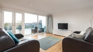 En moderne stue med en stor skydedør til en balkon, et fladskærms-tv og to lædersofaer.
