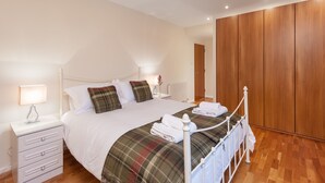 A bedroom with a bed, nightstands, a lamp, a wooden wardrobe, and a radiator. - Contemporary three-bedroom apartment with free parking space. Sleeps 5. (Edinburgh)