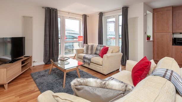 A modern living room with a sofa, a coffee table, a TV, and a kitchen area. - Contemporary three-bedroom apartment with free parking space. Sleeps 5. (Edinburgh)