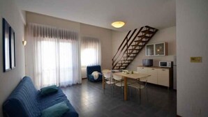 A living room with a sofa, a dining table, chairs, a staircase, and a kitchen area.