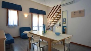 A dining area with a wooden table and chairs, a staircase, and a blue sofa.