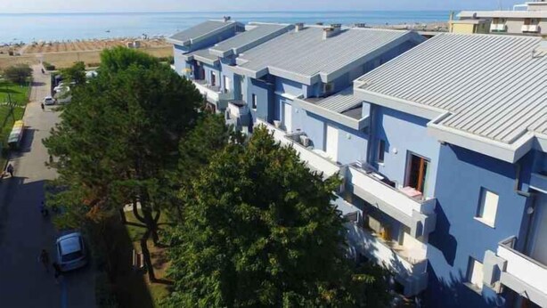 A row of modern buildings with flat roofs, likely part of a hotel or residential complex, adjacent to a beach.