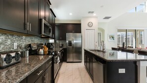A modern kitchen with dark cabinetry, granite countertops, stainless steel appliances, and a large island.