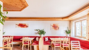 Un restaurant avec des tables en bois et des banquettes rouges rembourrées, des plantes en pot et des œuvres d’art accrochées aux murs.