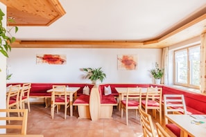 Ein Restaurant mit Holztischen, rot gepolsterten Sitzbänken, Blumentöpfen und Bildern an den Wänden.