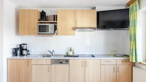 Une cuisine moderne avec des meubles en bois, un four à micro-ondes, un lave-vaisselle et une grande fenêtre agrémentée d’un rideau vert.