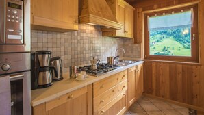 A kitchen with wooden cabinets, a gas stove, a coffee maker, and a view of a green landscape through a window. - MAS DE LA BOLP,  MOUNTAIN CHALET (Rabbi)