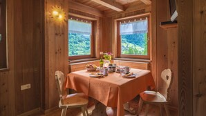 A wooden cabin with a dining table set for breakfast, two windows with curtains, and a television mounted on the wall. - MAS DE LA BOLP,  MOUNTAIN CHALET (Rabbi)