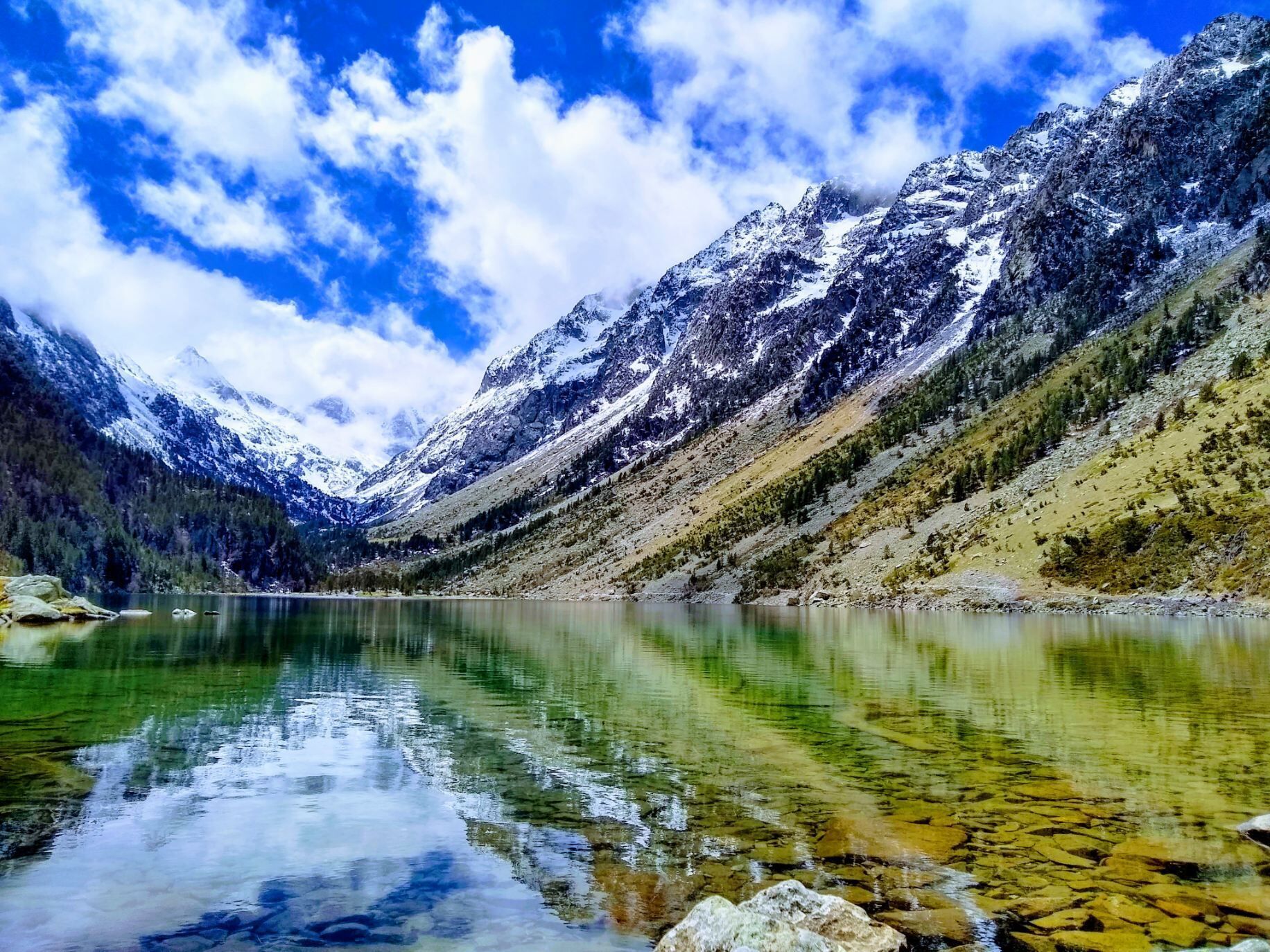 Een bergmeer met helder water dat het omliggende landschap weerspiegelt, omringd door besneeuwde bergen en dicht bos.