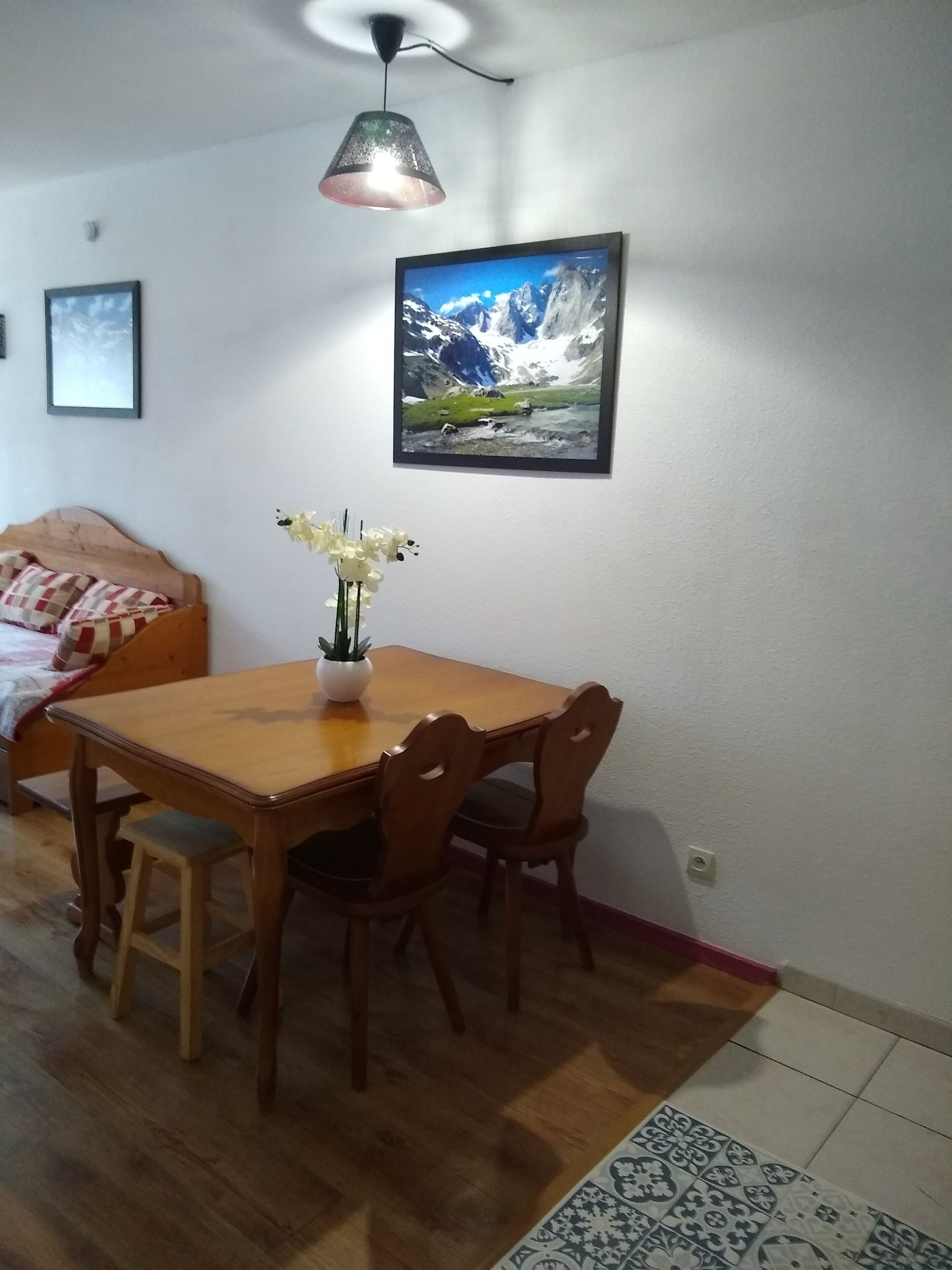 A dining area with a wooden table and chairs, a vase with flowers, and a framed picture on the wall.
