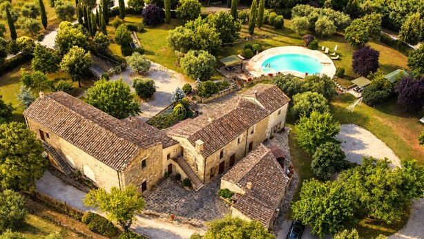 Un patio con piscina, edificios de piedra y abundante vegetación.