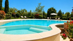 Piscina con sillas de descanso y un jacuzzi, rodeada de exuberante vegetación y árboles.