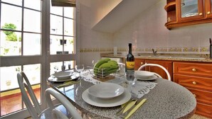 Un coin repas avec une table dressée pour deux personnes, une bouteille de vin et un panier de bananes.