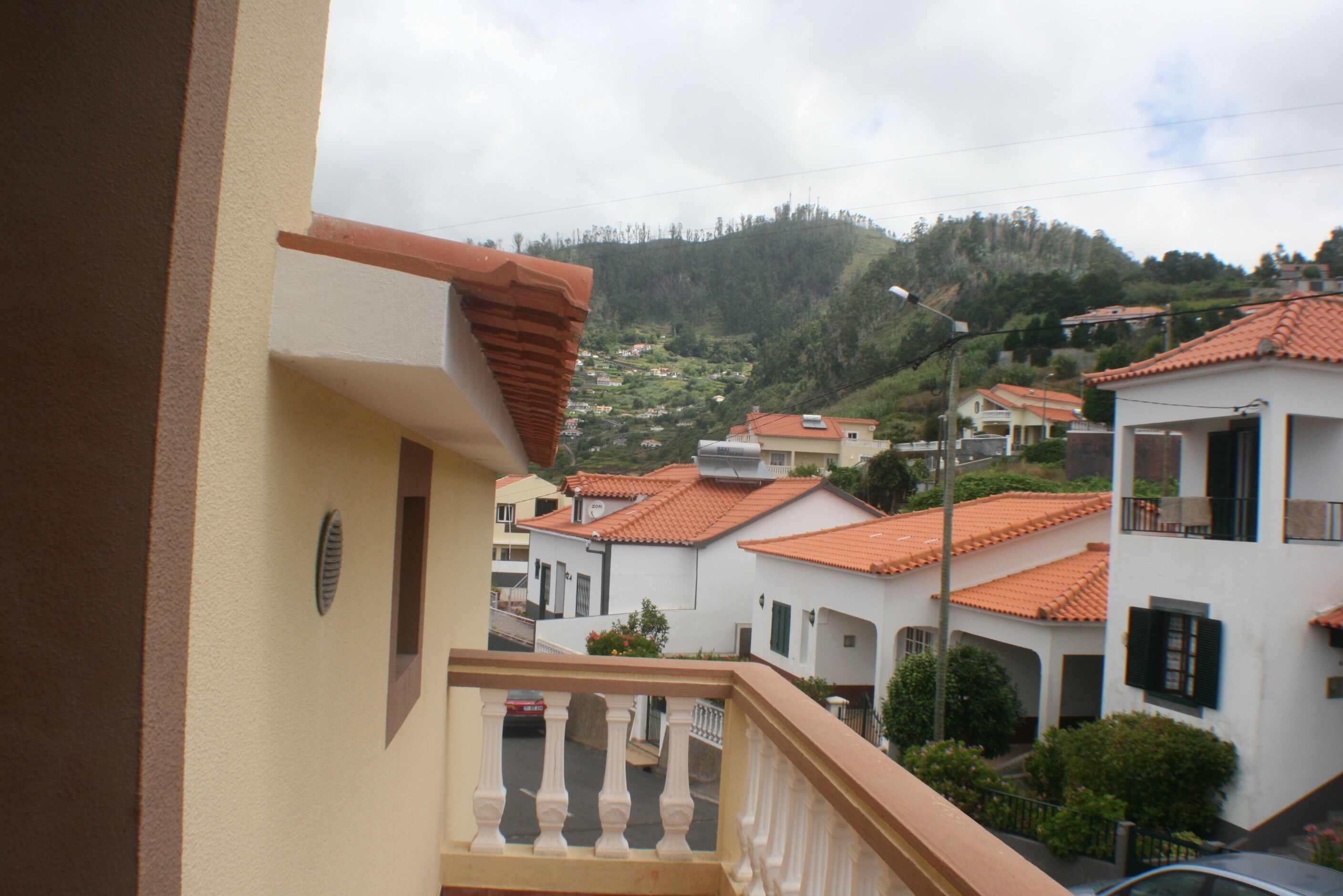Et boligområde med huse med terracotta-tag, en balkon med gelænder og en gade med parkerede biler.