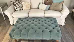 A tufted ottoman in teal fabric with a decorative border, placed in front of a white leather sofa with various cushions. - Historic downtown home a block from king st and 10-15 mins to the beach!  (Charleston)