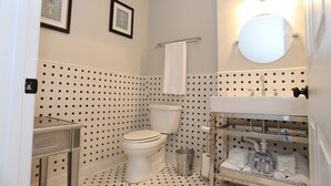 A bathroom with a toilet, sink, and mirror. There are two framed pictures on the wall, a towel rack, and a trash can. - Historic downtown home a block from king st and 10-15 mins to the beach!  (Charleston)
