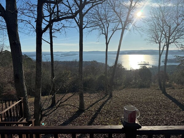 A wooden deck overlooking a lake with trees and a distant bridge.