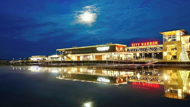 Un edificio sul lungomare con un cartello 'City Harbor', un riflesso nell'acqua e un grande albero di Natale illuminato.