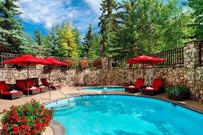 A swimming pool with red umbrellas, lounge chairs, and a stone wall. - Charlie Rentz: Best Location BC Village! Creekside Unit, Walk to Lifts, Ski School, Dining (Beaver Creek)