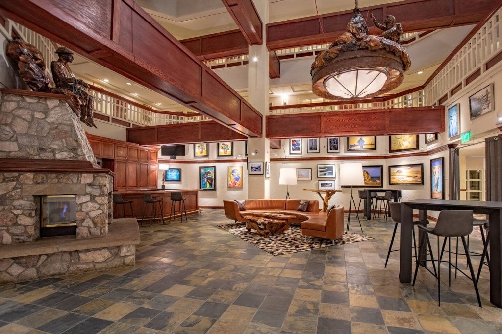 A spacious lobby with a stone fireplace, wooden ceiling beams, a large chandelier, and a seating area with a coffee table.